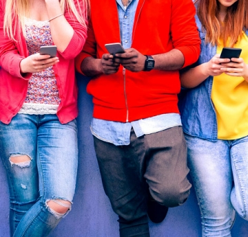 Students leaning on a wall with smart phones