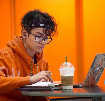 Student in an orange sweatshirt with a laptop