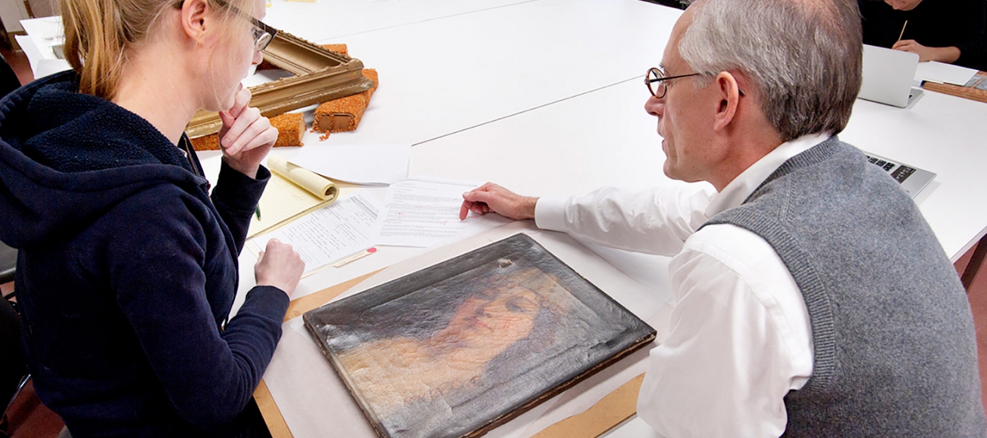 Art Conservation student and faculty inspecting a painting.